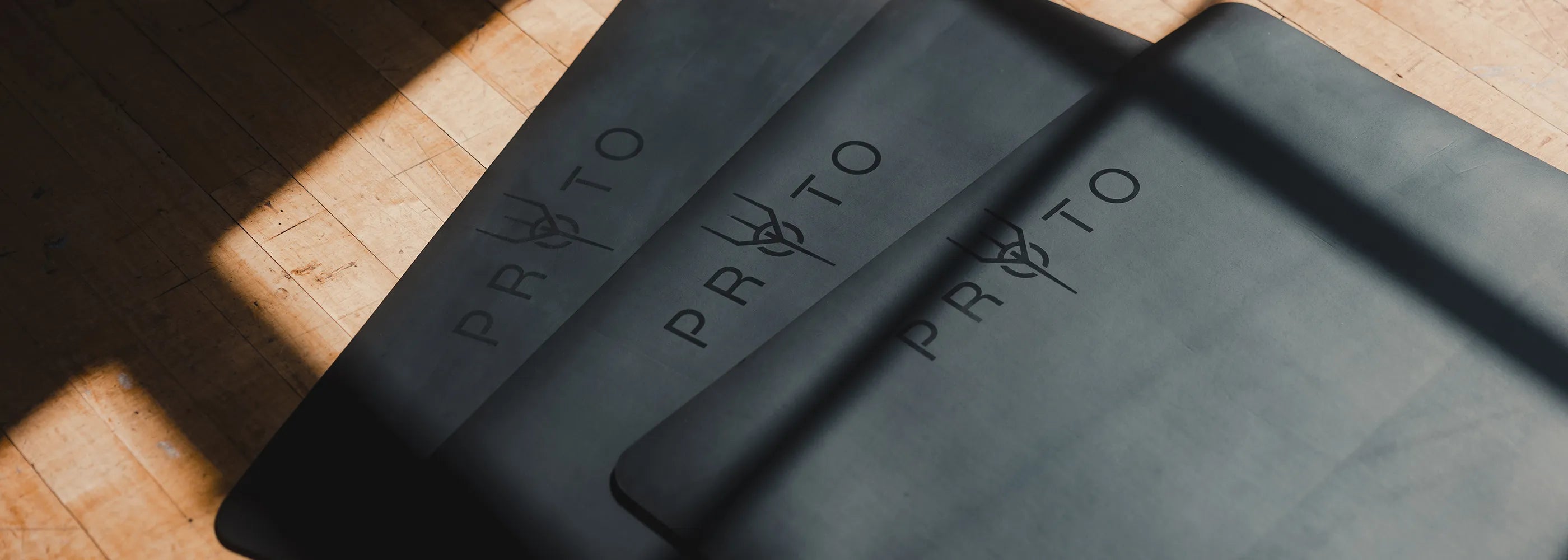 Three black PROTO YOGA MATS on a wooden surface